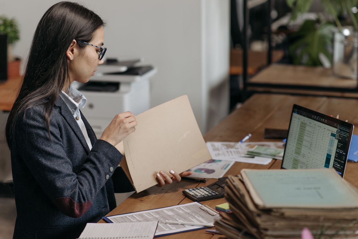 Recruiter sorting through printed resumes and files beside a laptop