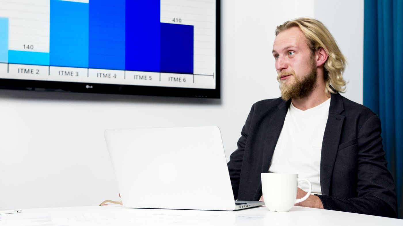 Analyst at a laptop in front of a wall screen showing a bar chart
