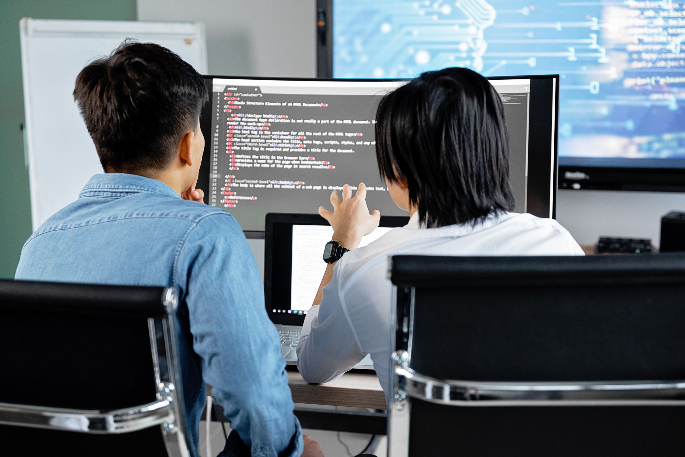 Two developers reviewing application code together on a large monitor