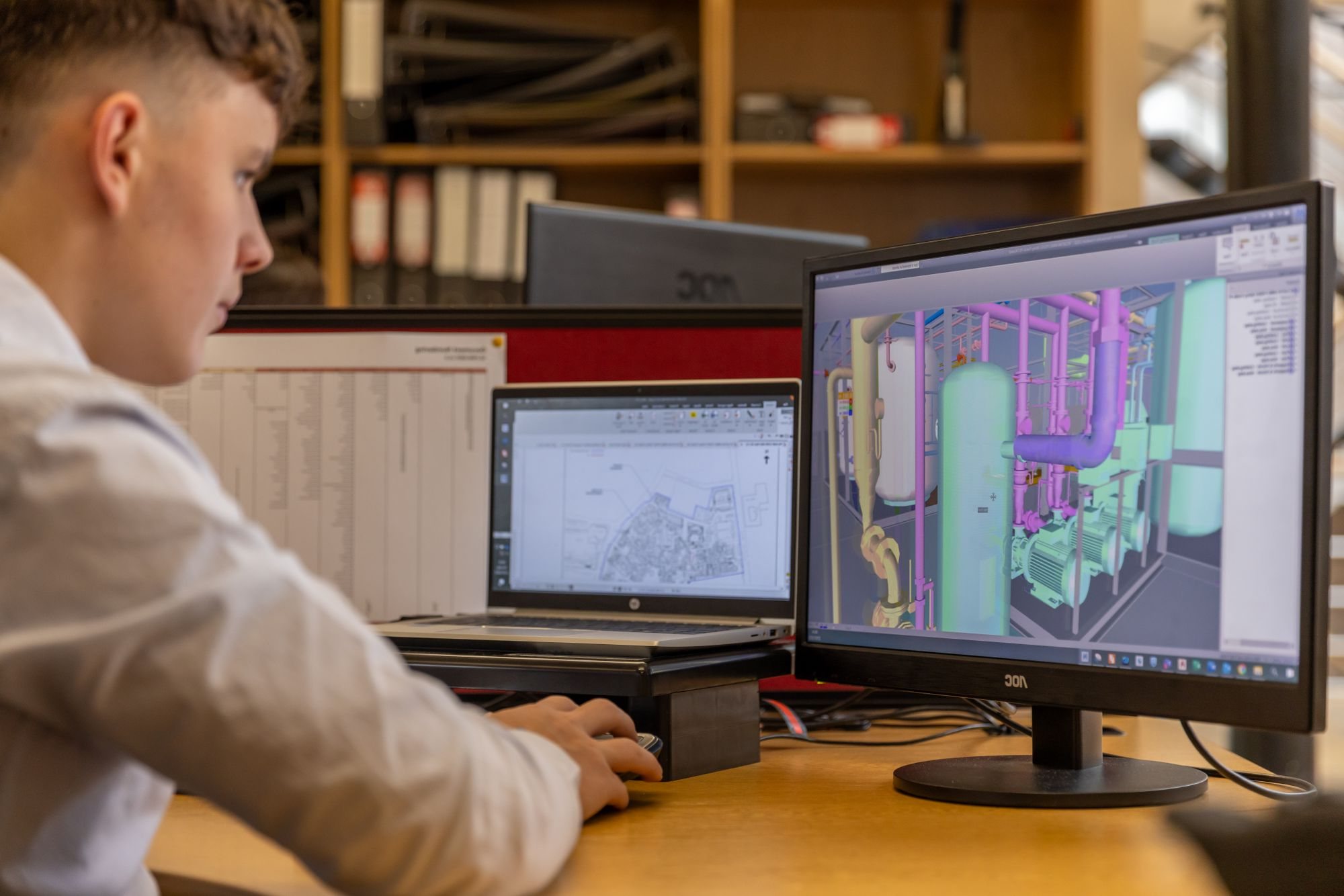 Engineer reviewing a 3D model of plant pipework on two monitors