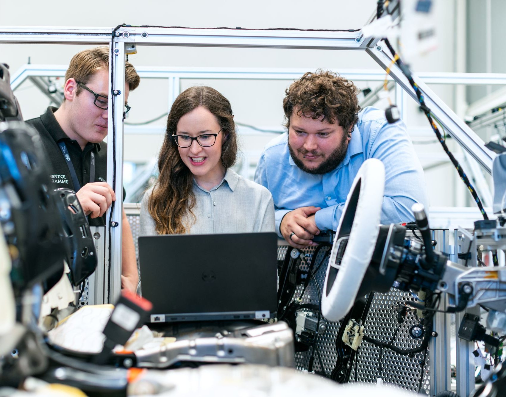 Three engineers reviewing data on a laptop beside test equipment in a bright lab