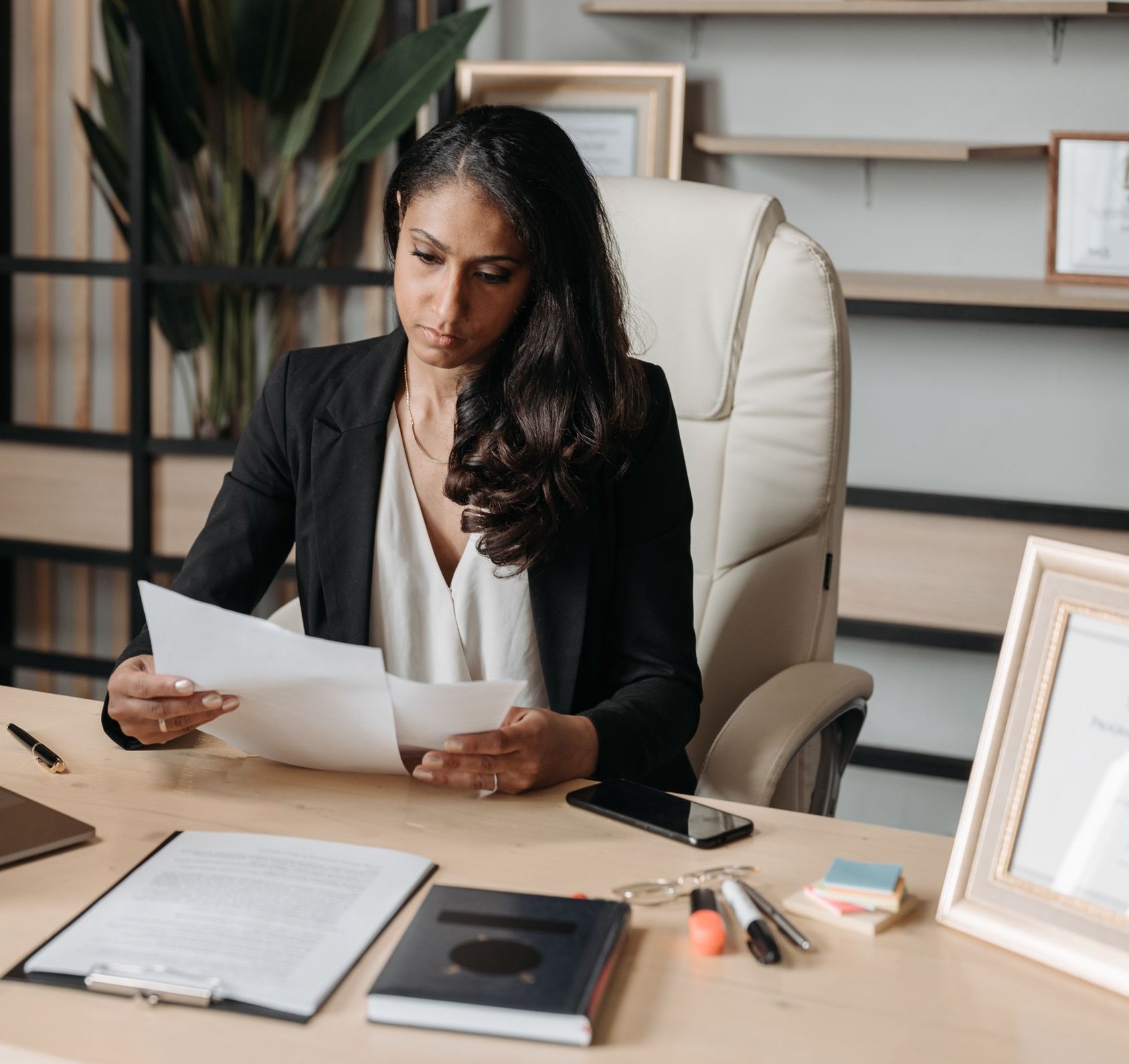 Manager reading a printed report at her desk beside an open laptop