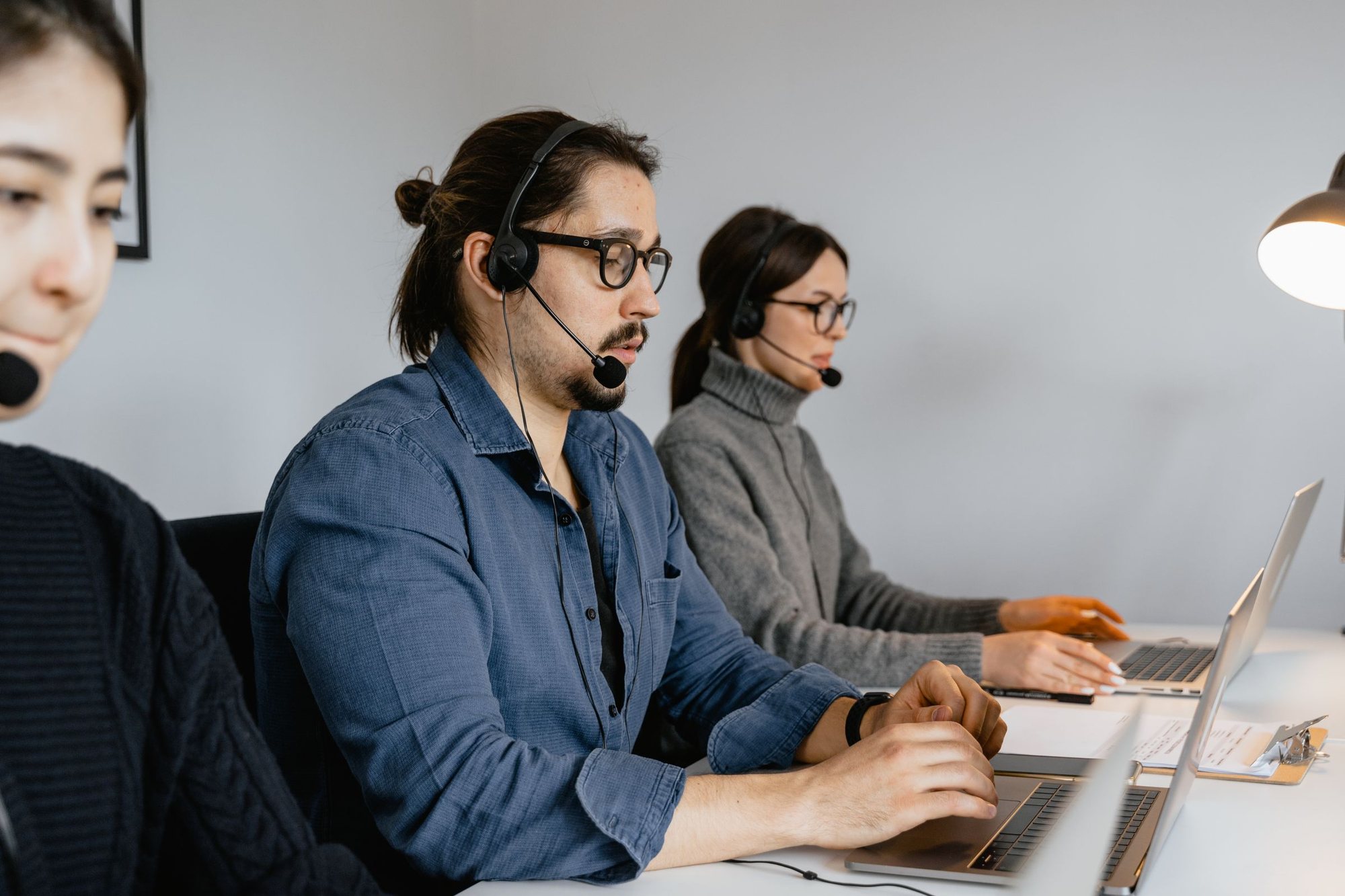 Sales representatives with headsets working at laptops in a bright office