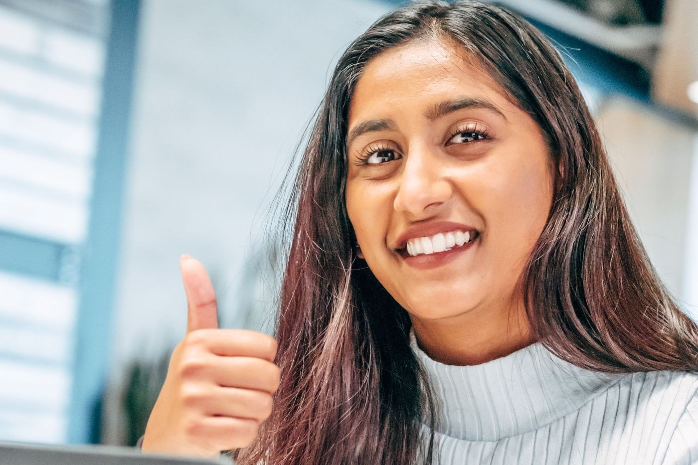 Smiling employee giving a thumbs up at her desk as an employer brand ambassador