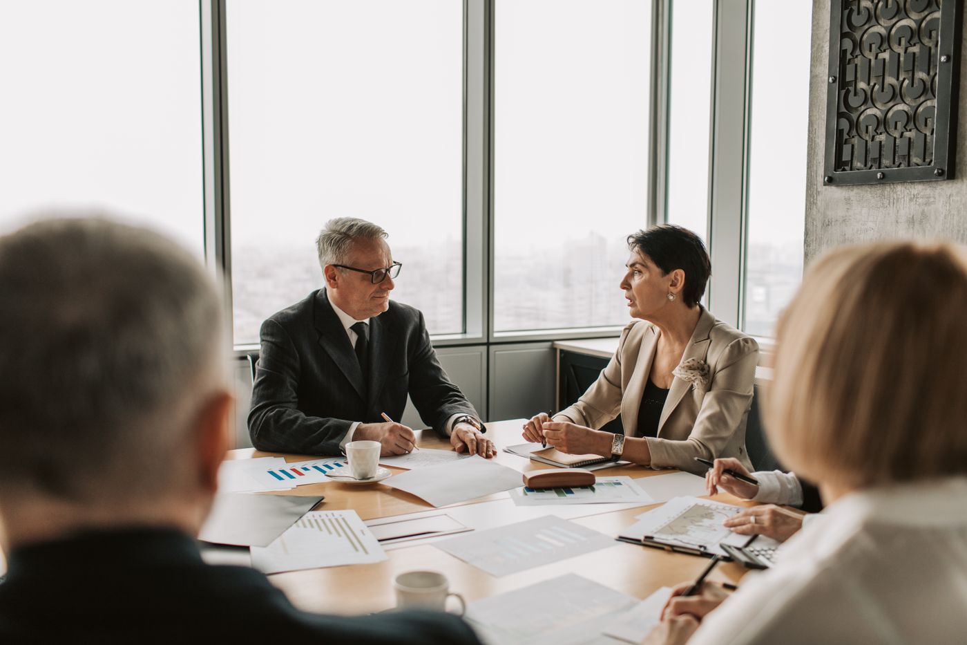 Leadership team in discussion around a boardroom table by tall windows