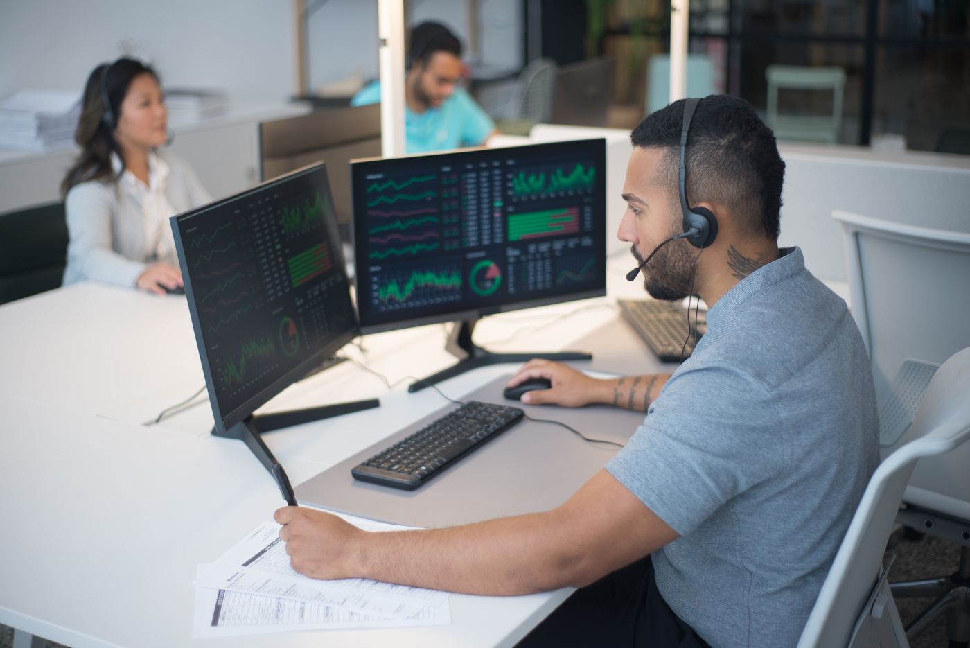 Support engineer with a headset monitoring dashboards across two screens