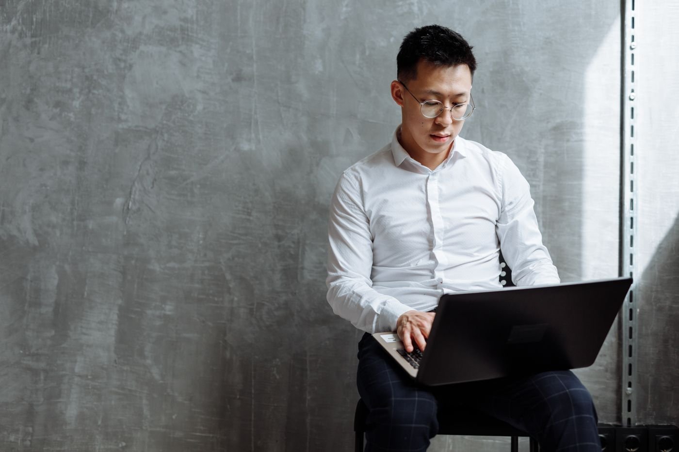 Engineer working on a laptop against a plain concrete wall