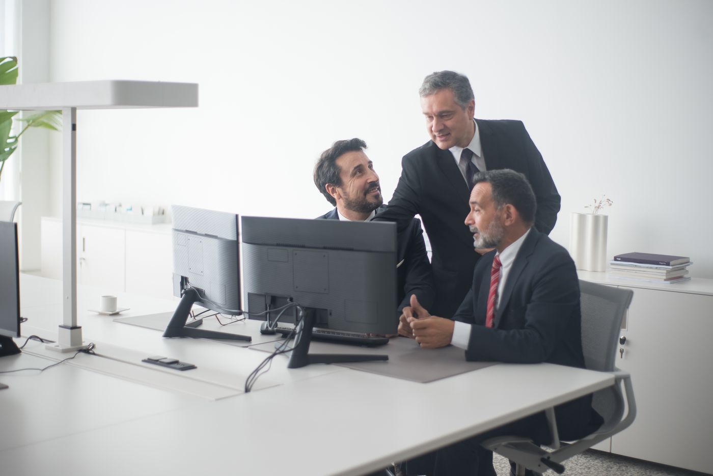 Three senior executives reviewing work together at a desk with monitors