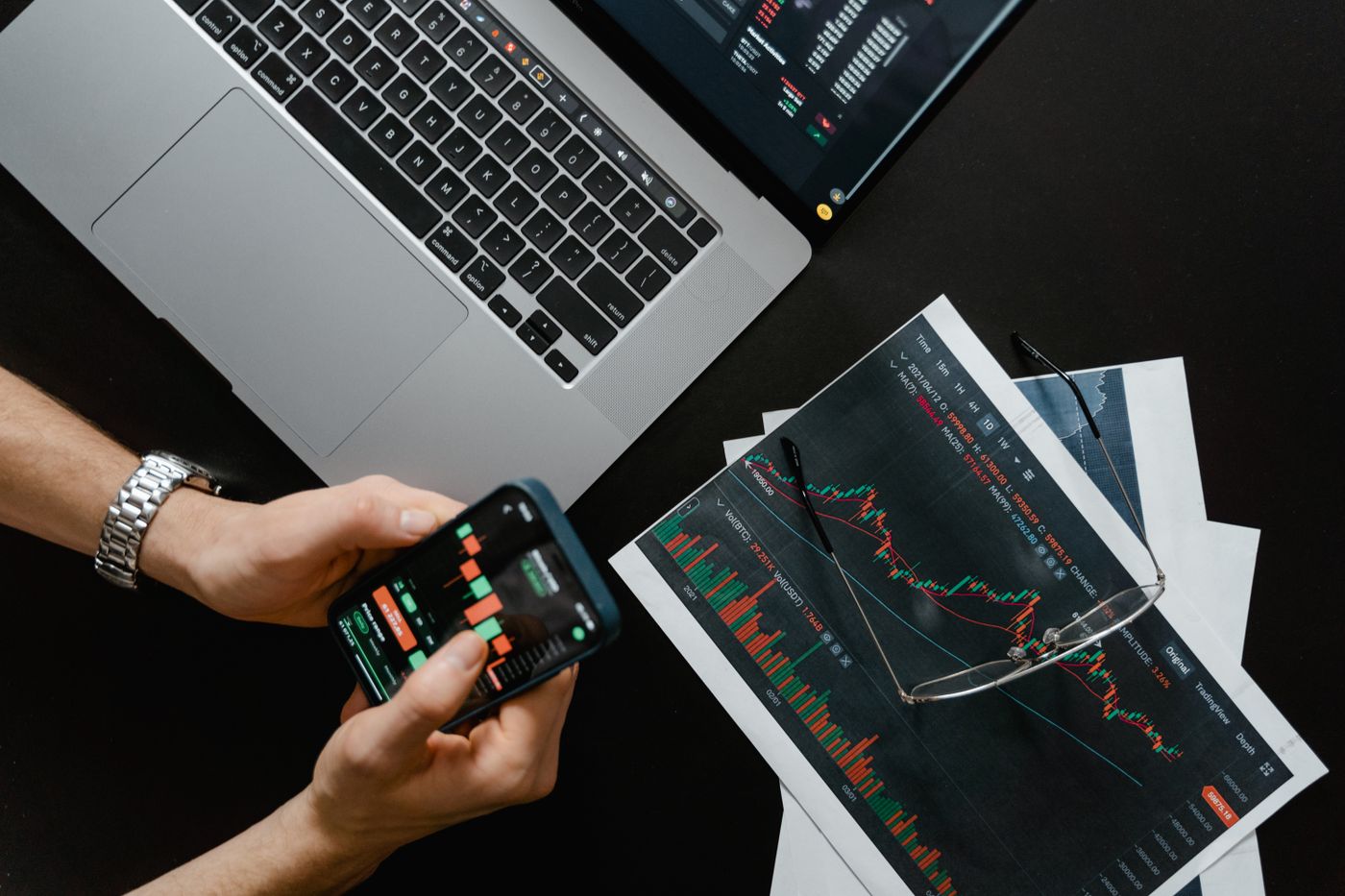 Financial charts and documents beside a laptop and phone