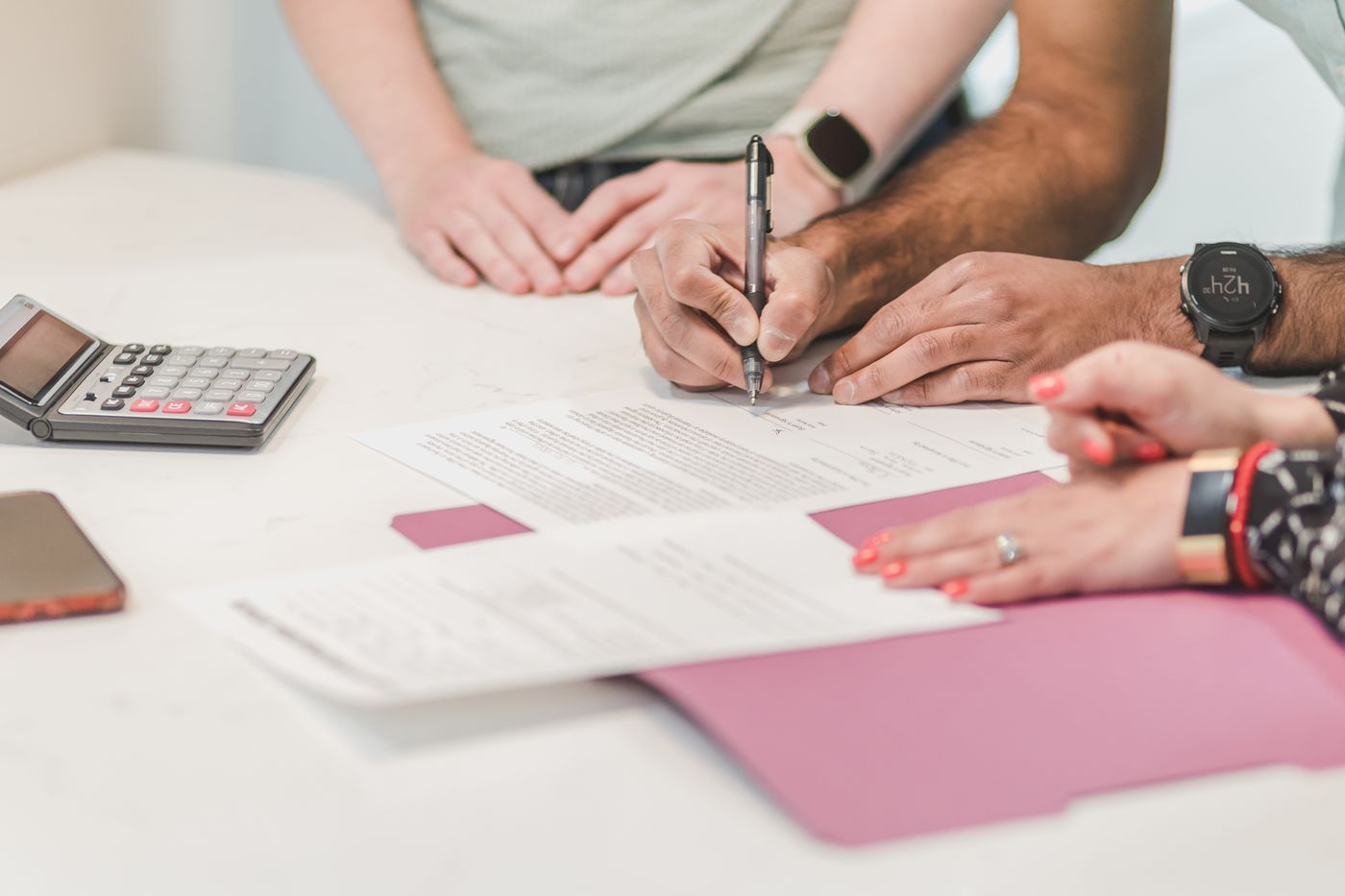 People signing documents at a table beside a calculator