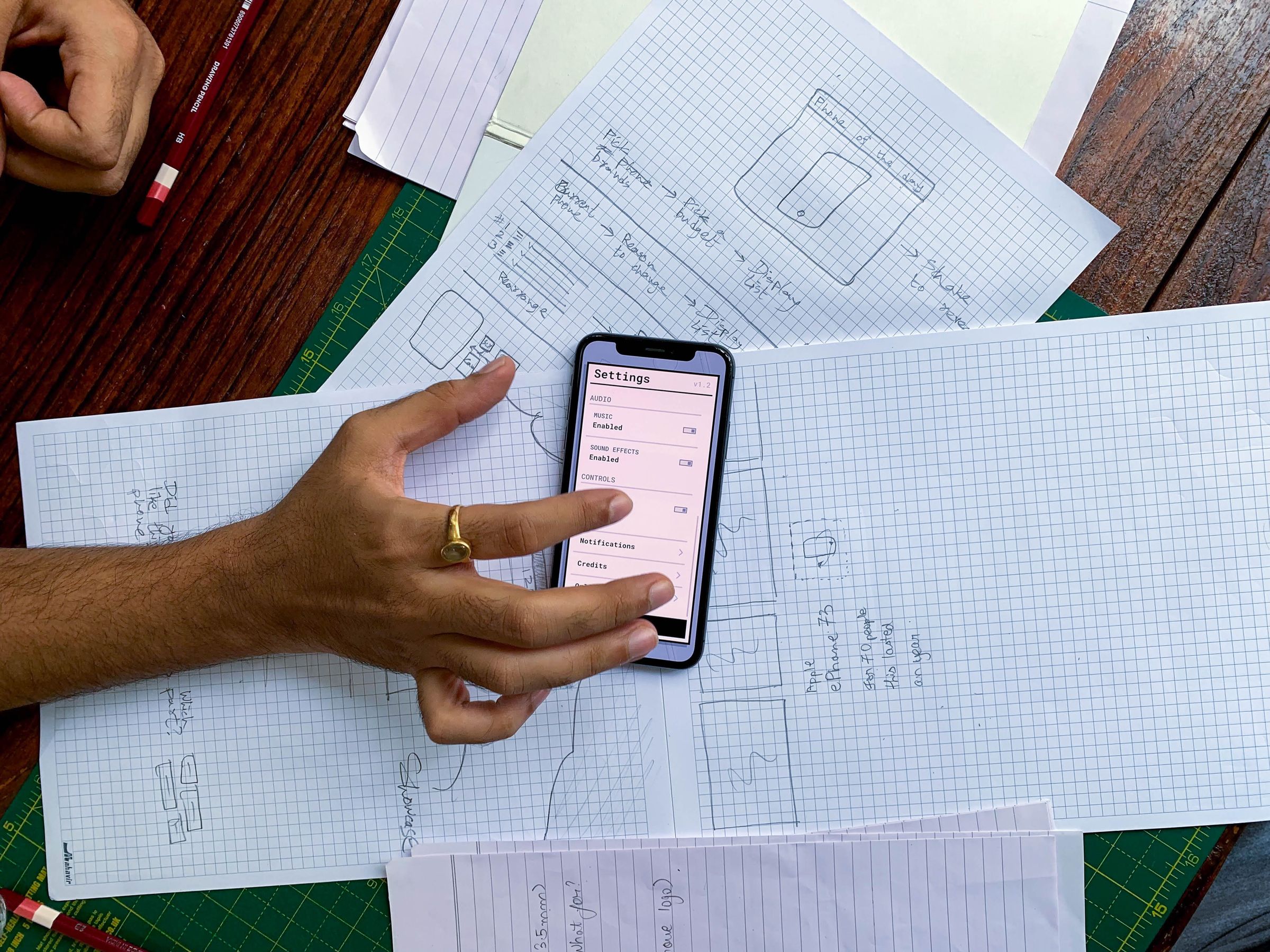 Digital product development from idea to product, shown as a finished app on a phone held over its paper wireframes
