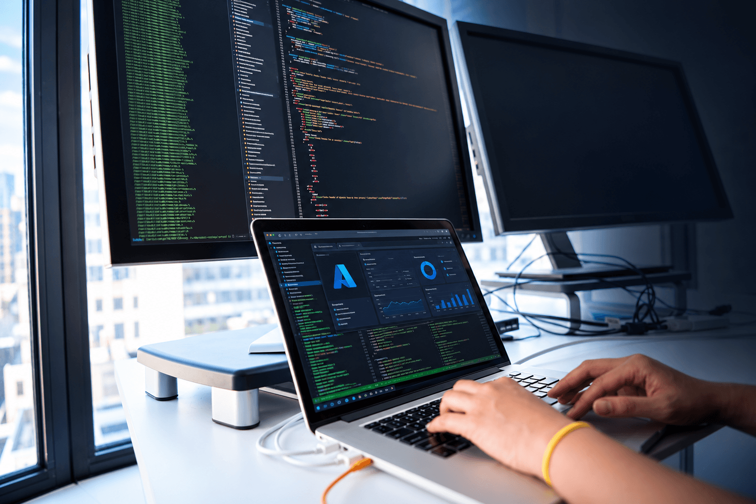 Azure cloud engineering workstation with code on monitors and an Azure dashboard on a laptop