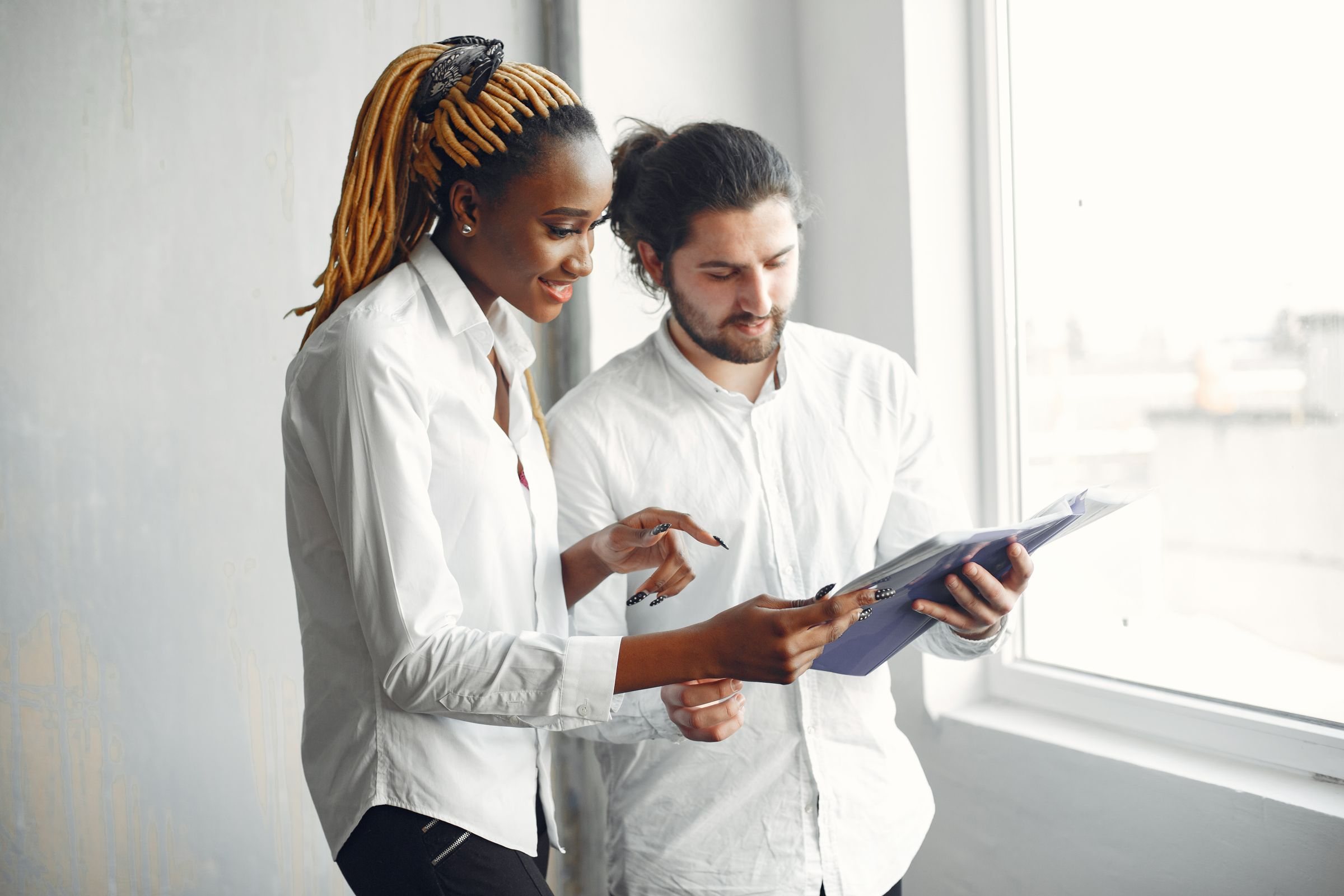 Two colleagues reviewing platform work on a tablet beside a bright office window