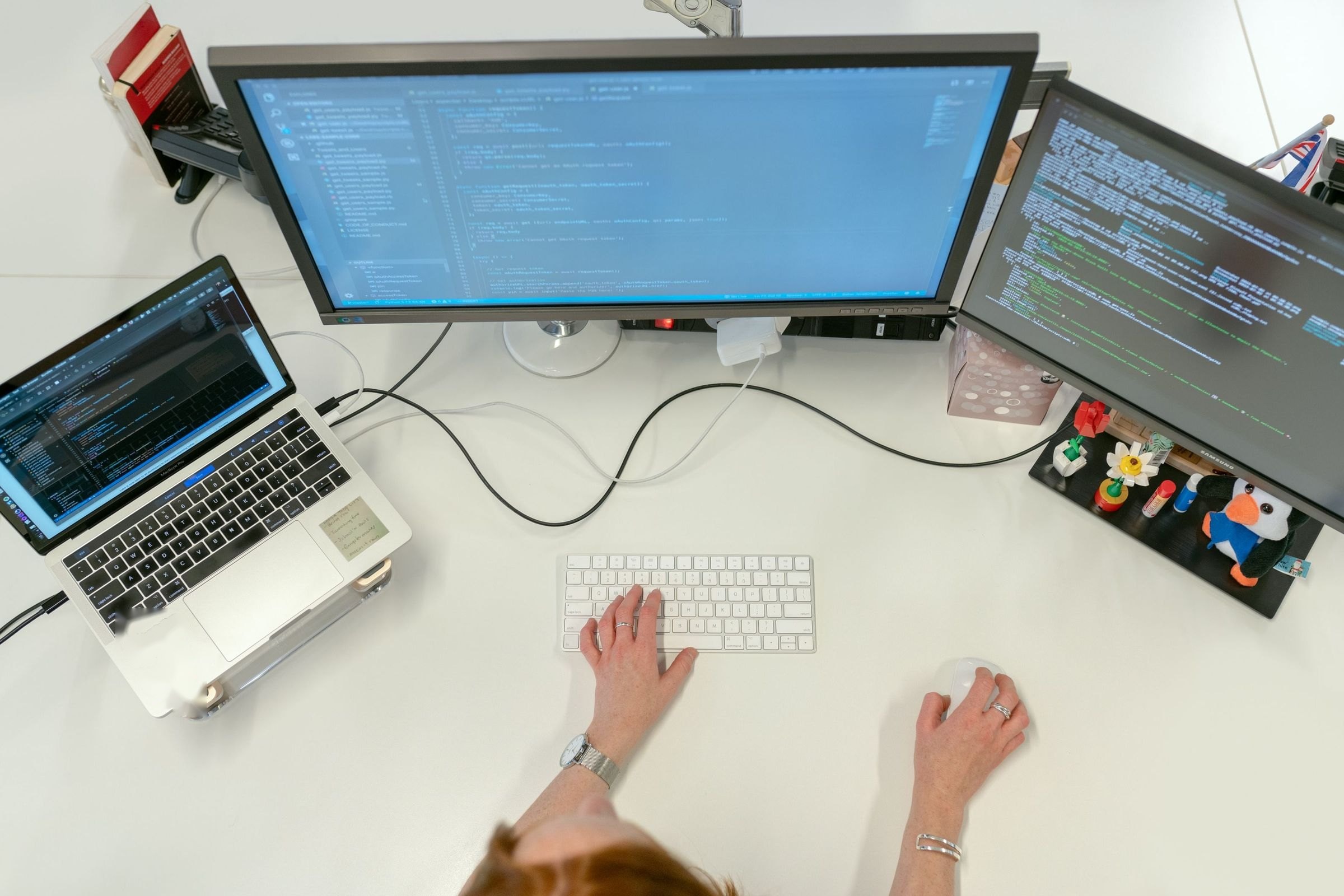 Data engineer working across a laptop and two monitors of pipeline code, seen from above