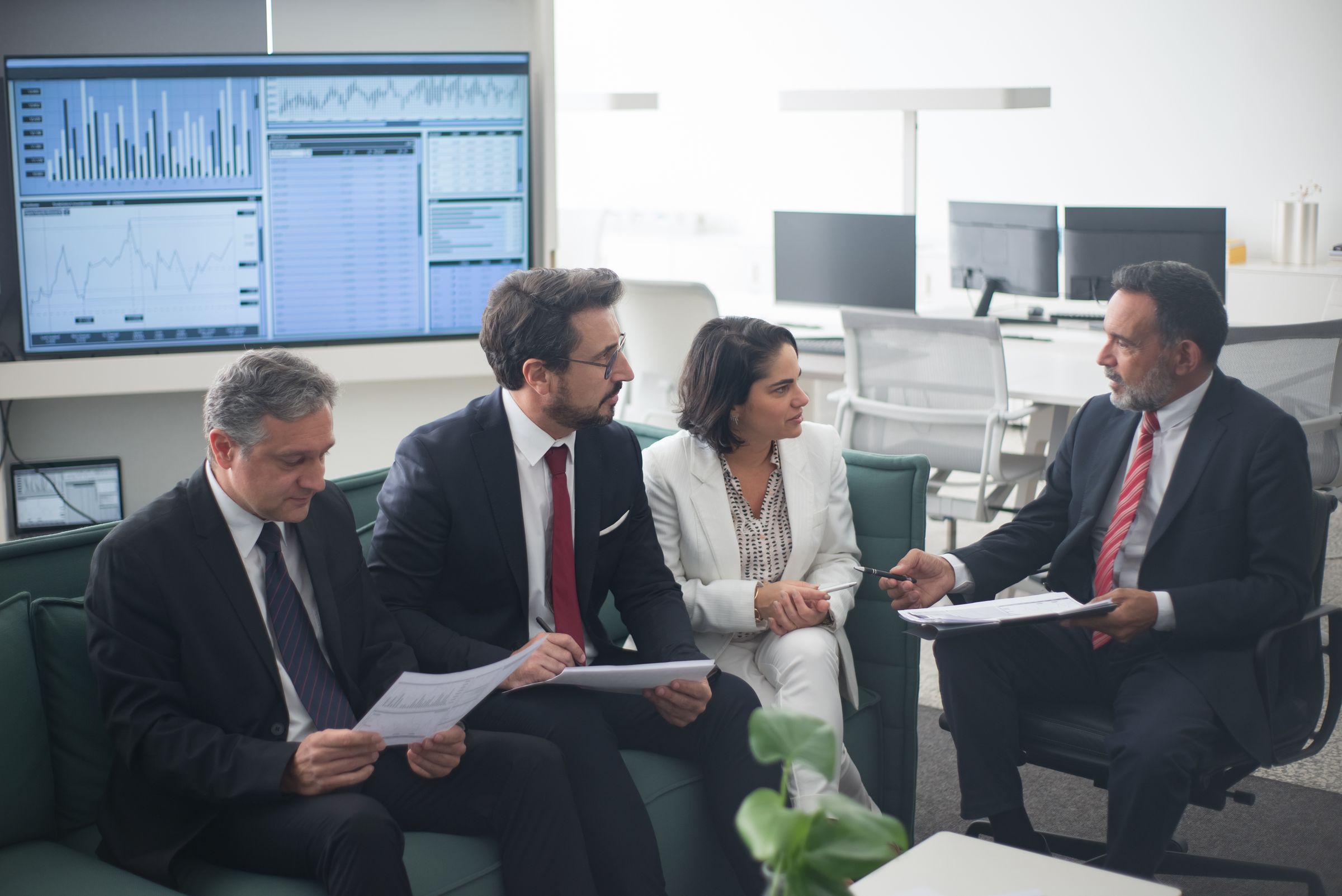 Business leaders discussing enterprise operations below a data dashboard in a bright office