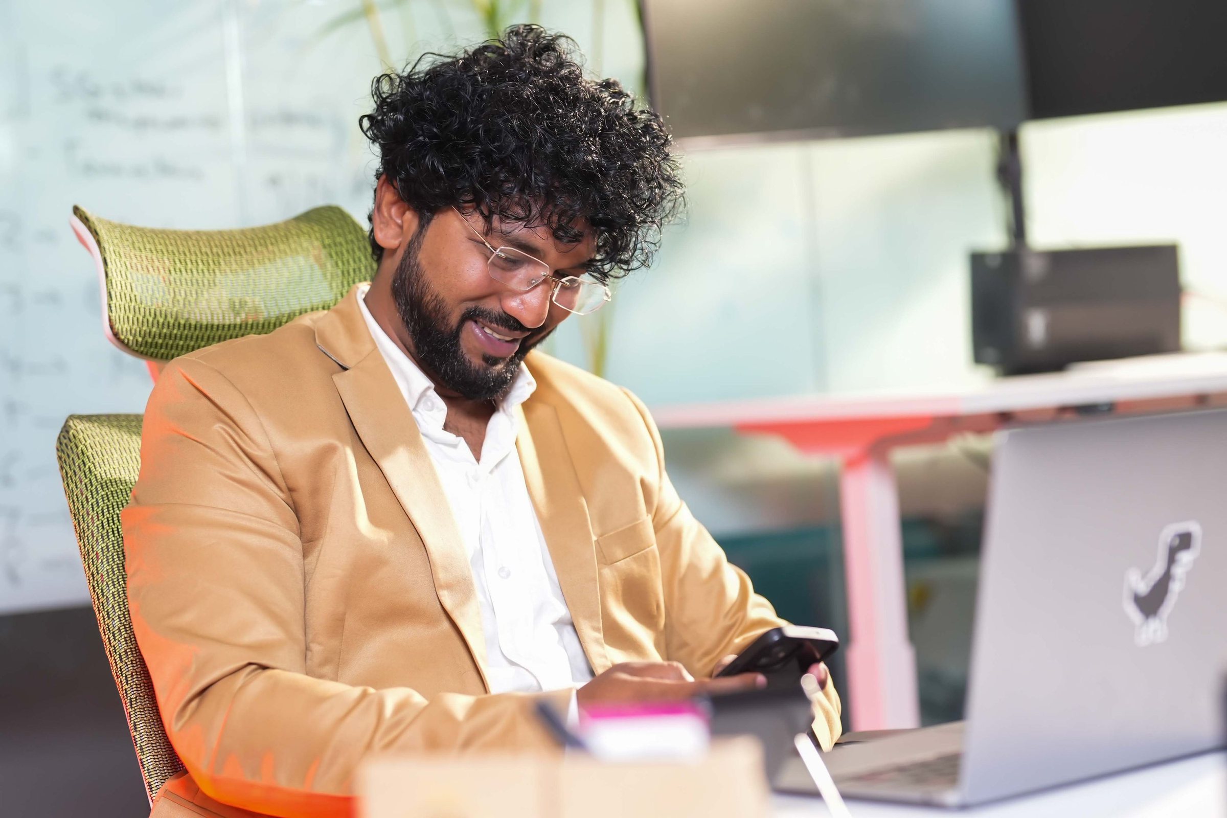 Performance marketer checking campaign results on his phone beside a laptop in a bright office