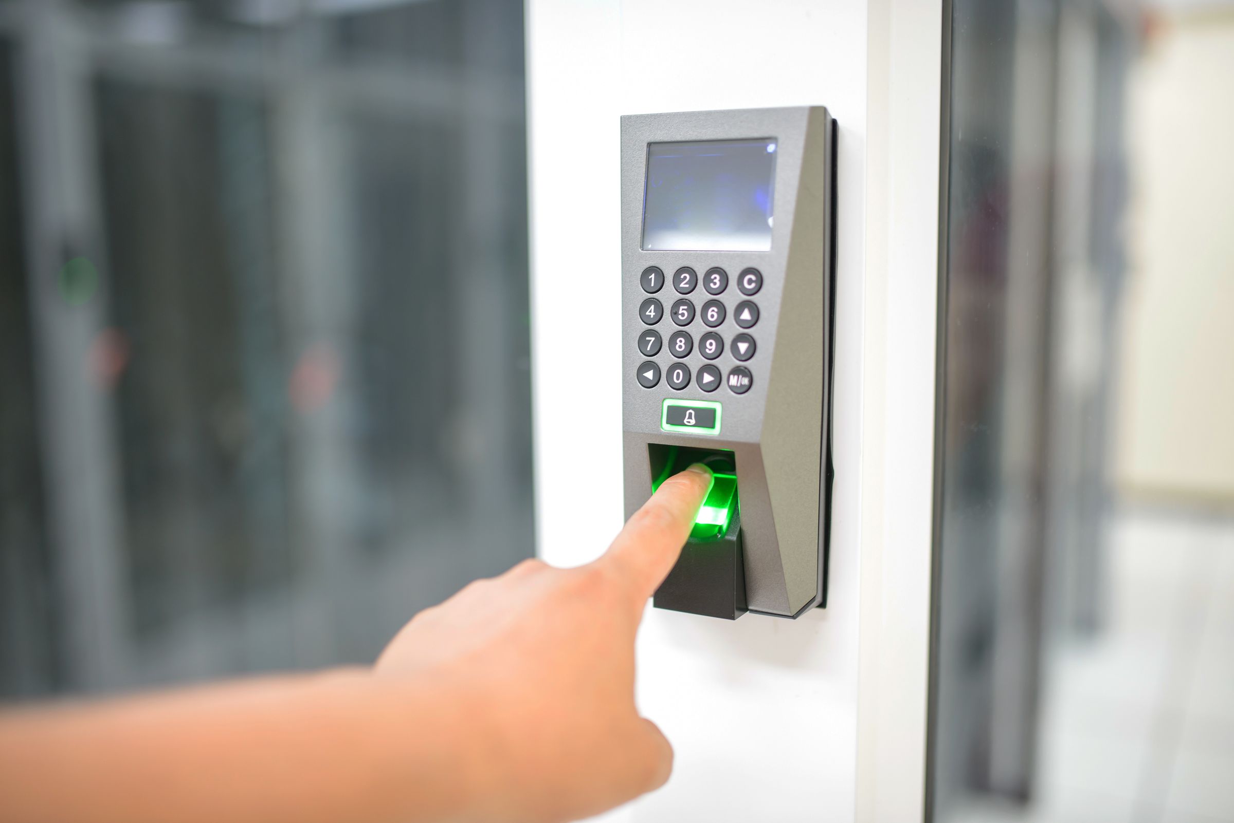 Finger on a biometric access scanner beside a data center door