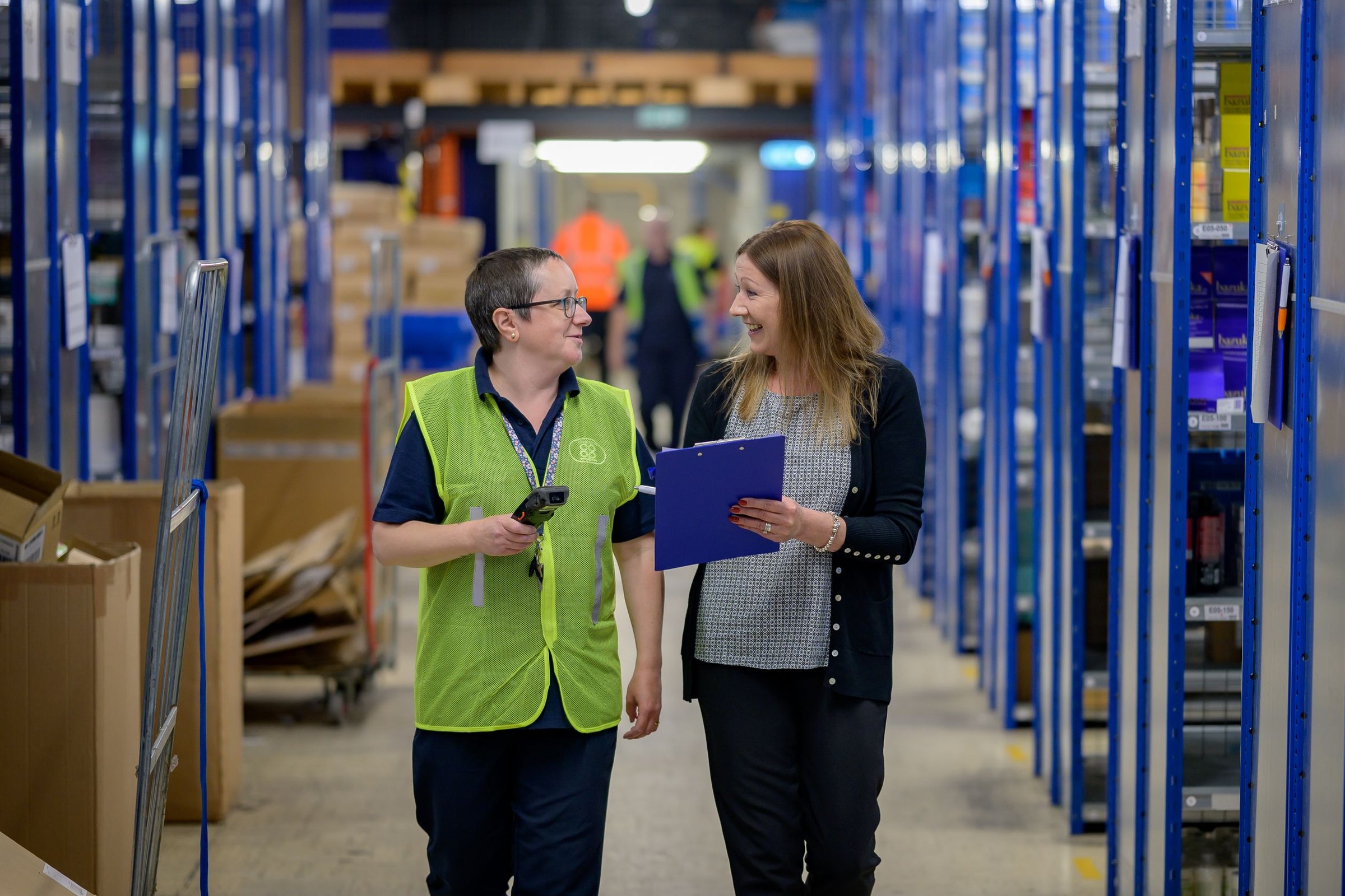 Procurement manager walking a supplier warehouse aisle with an operations colleague