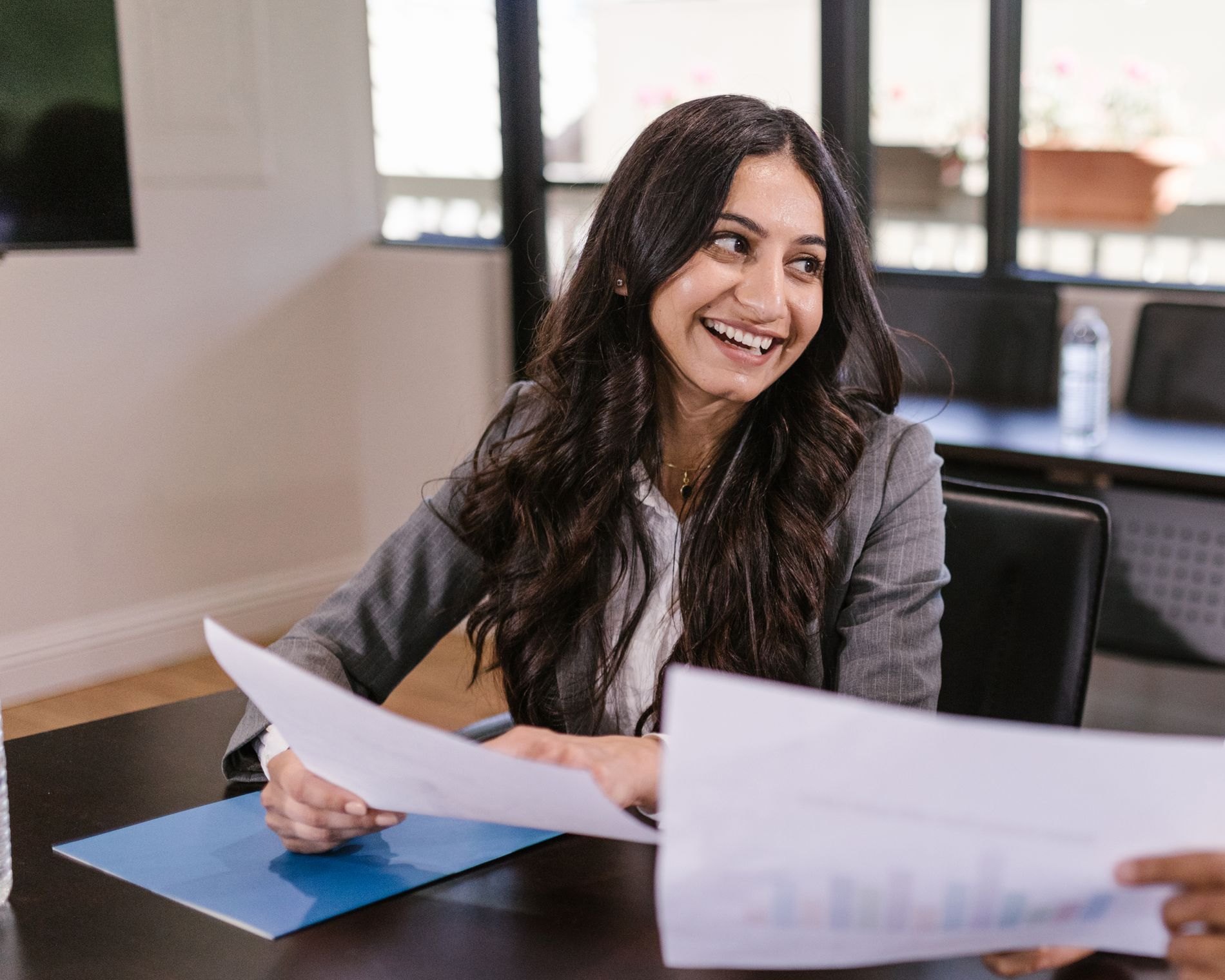 Revenue team member smiling as she reviews pipeline reports with a colleague in a bright meeting room