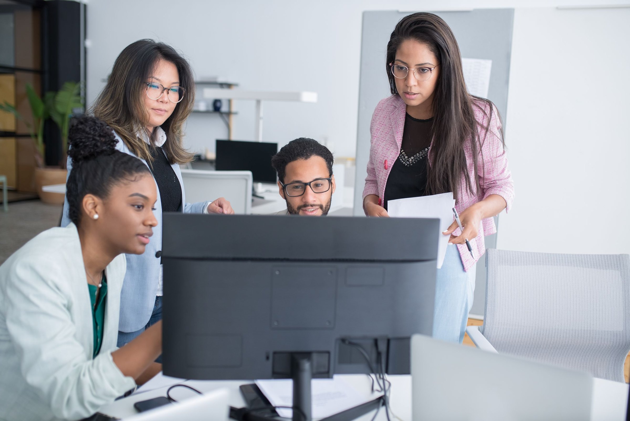 Engineering team gathered around a monitor, reviewing work together in a bright office