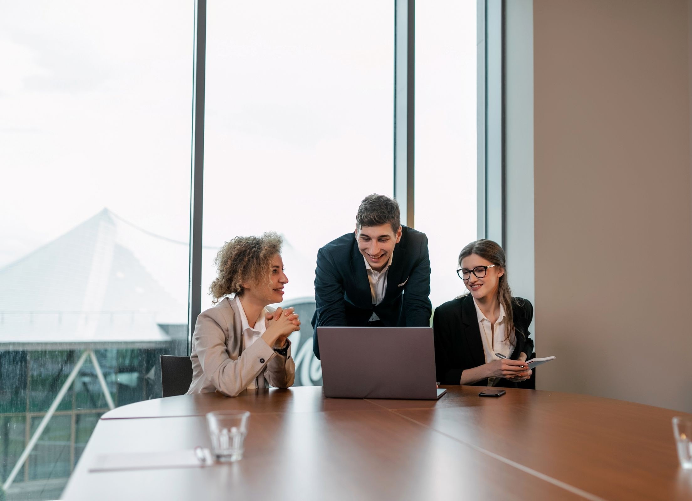 Three colleagues discussing enterprise applications around a laptop in a bright, window-lit meeting room