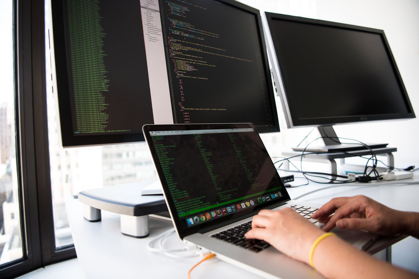 Developer writing code across a laptop and two large monitors