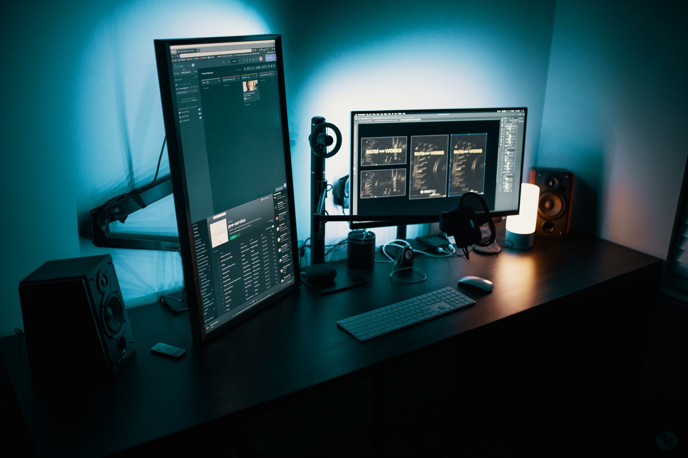Monitors on an adjustable arm at a desk lit in teal