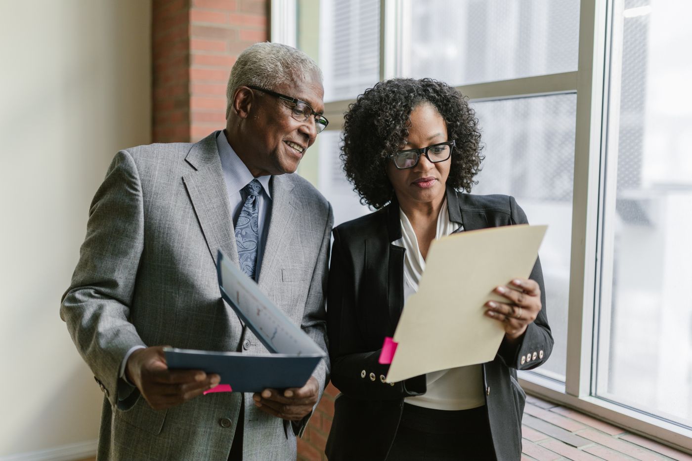 Two senior professionals reviewing a document together by an office window