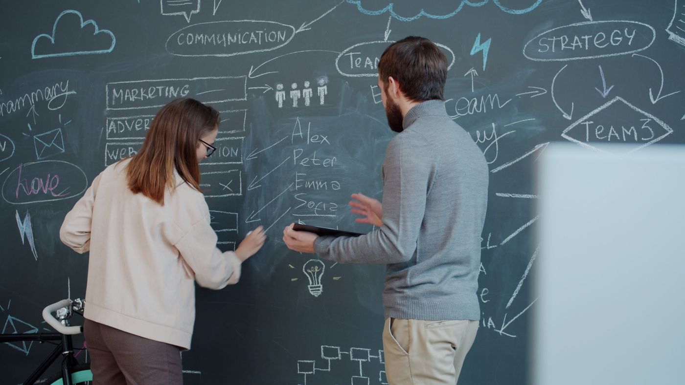 Two colleagues sketching a sales stack architecture on a chalkboard