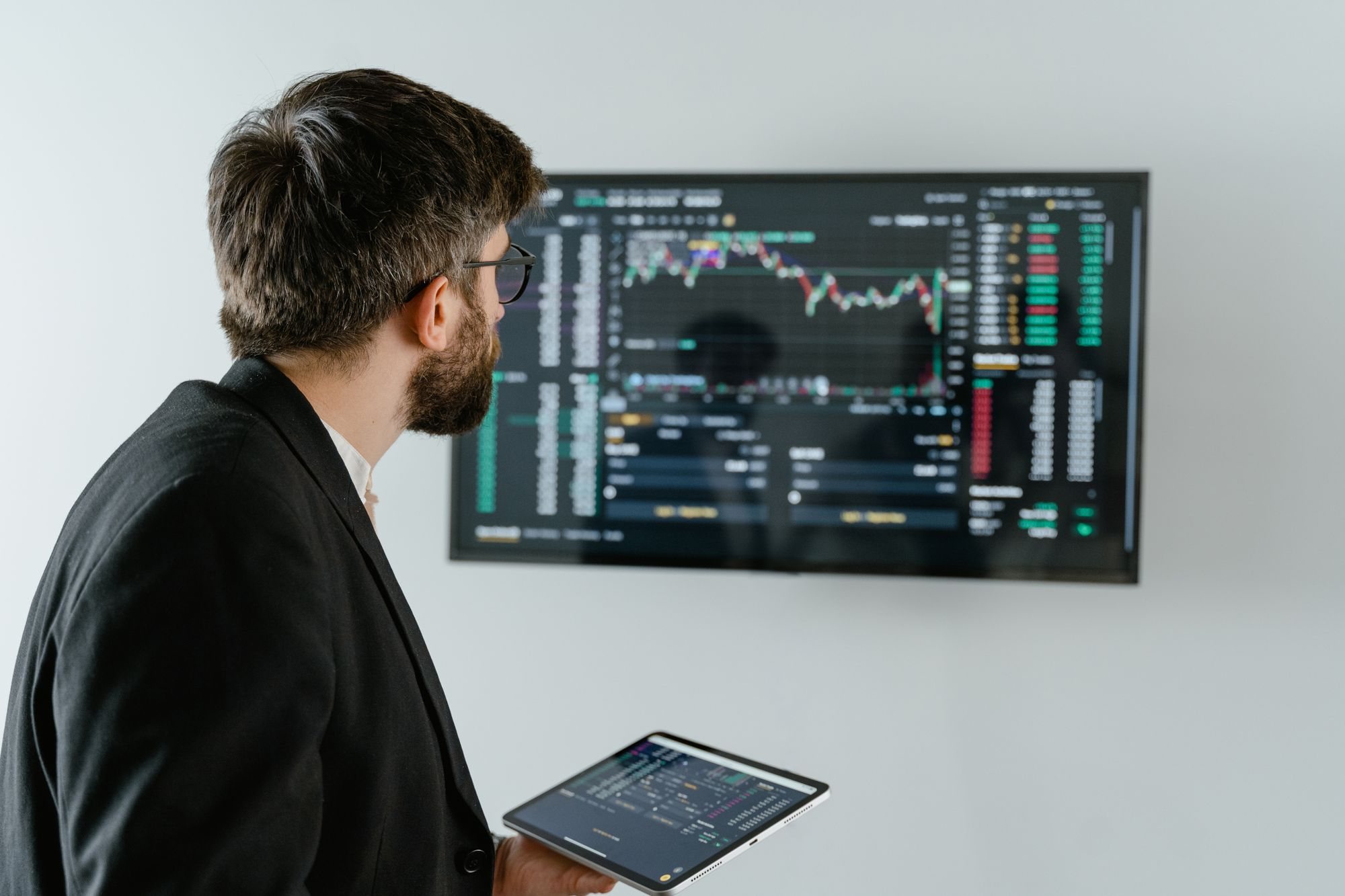 Analyst holding a tablet in front of a wall screen of live data charts