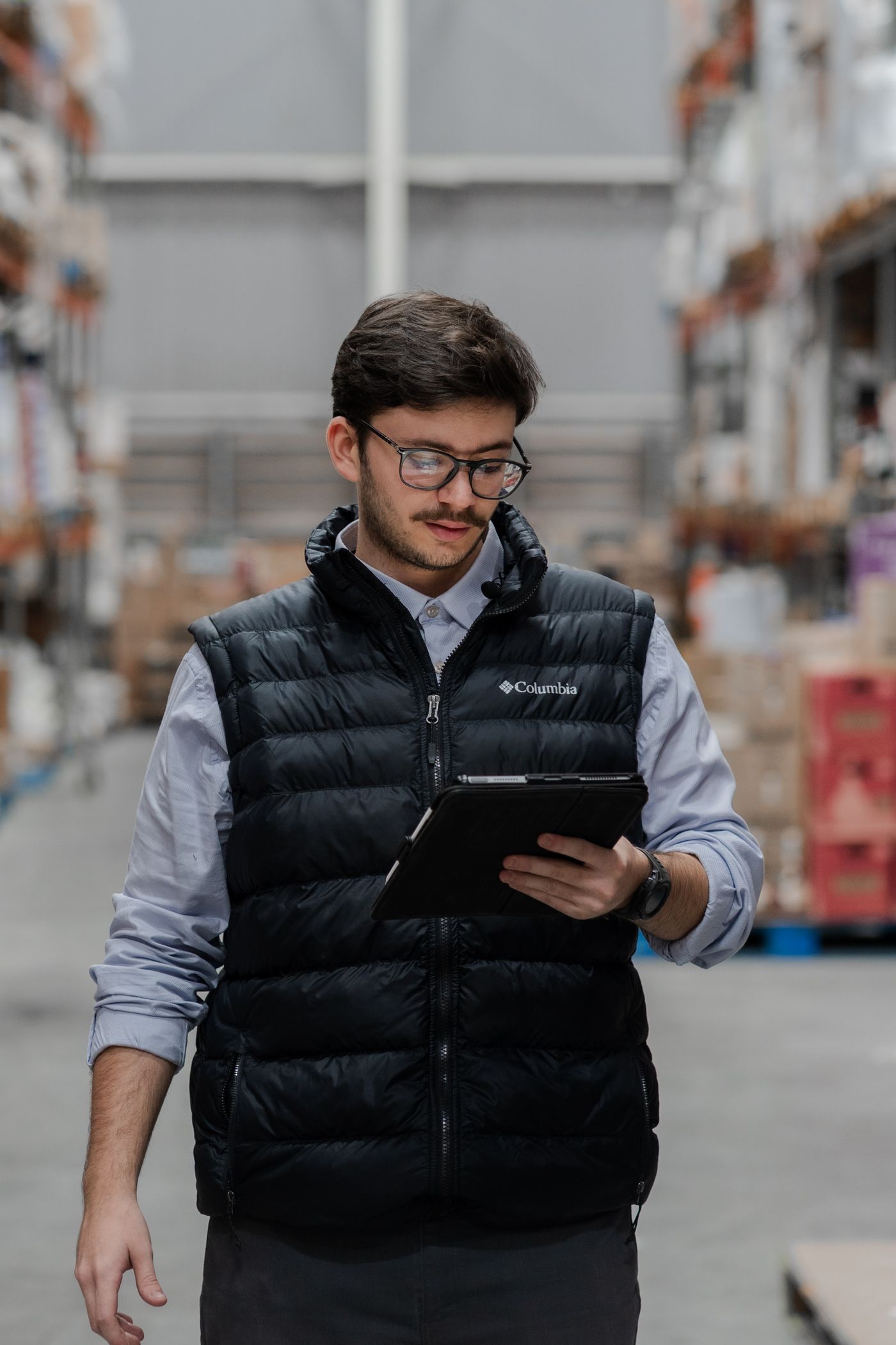 Supply chain planner walking a warehouse aisle with a tablet